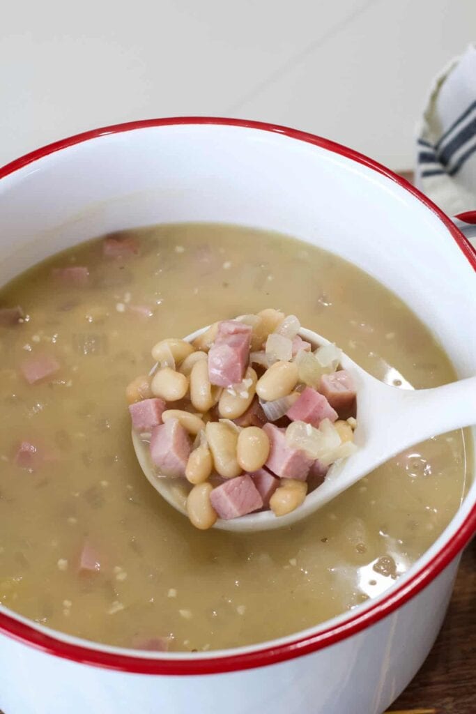 A spoonful of 30-Minute White Beans with Ham held over a pot filled with the remaining beans.