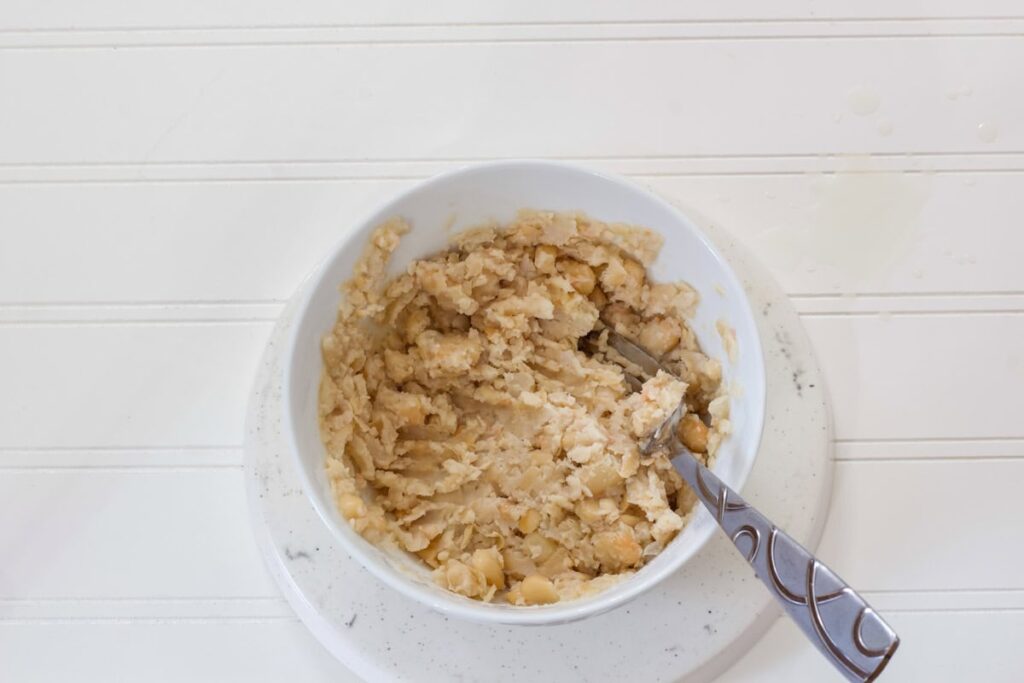 One cup of the white beans mashed in a bowl.