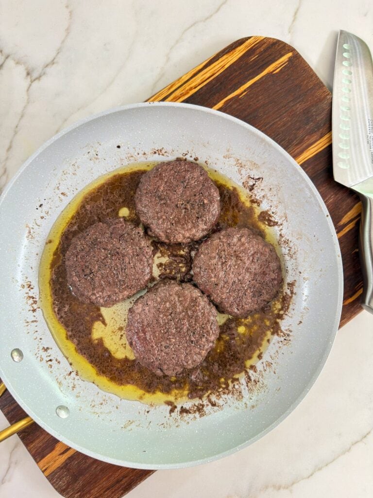 Four hamburger patties in the skillet they were cooked in.