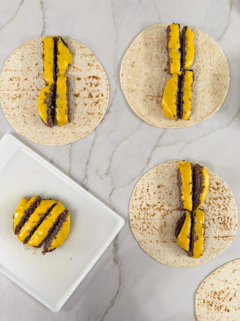 The hamburger patties after cheese has been added and they've each been cut into four strips.