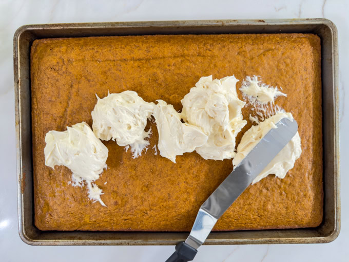 Piles of cream cheese frosting on the top of the pumpkin cake, ready to be spread.