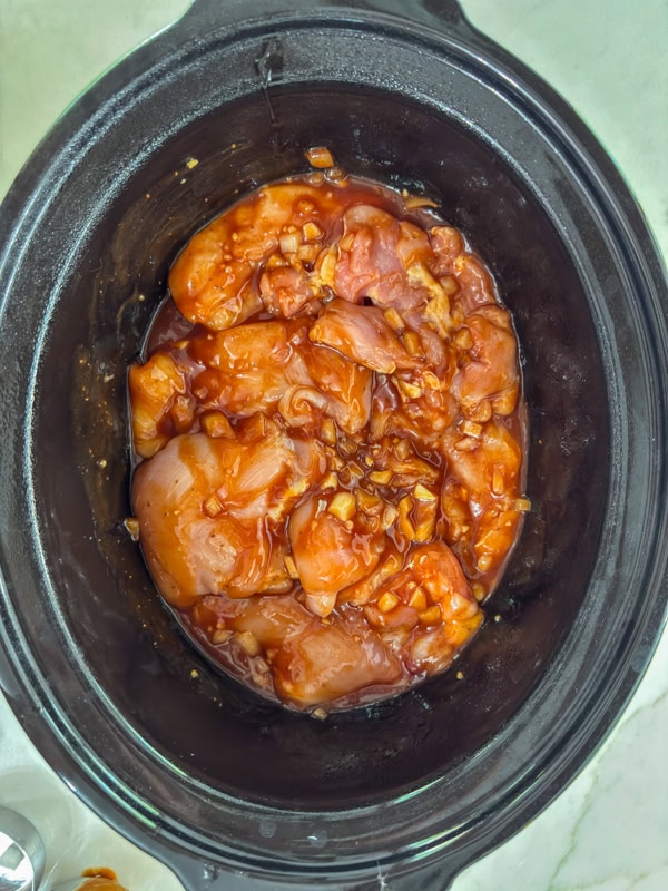 The raw chicken and other ingredients in the crockpot ready to be cooked.