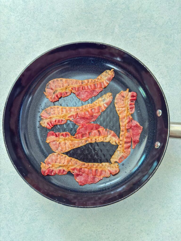 The pre-cooked bacon after being crisped up in a pan.