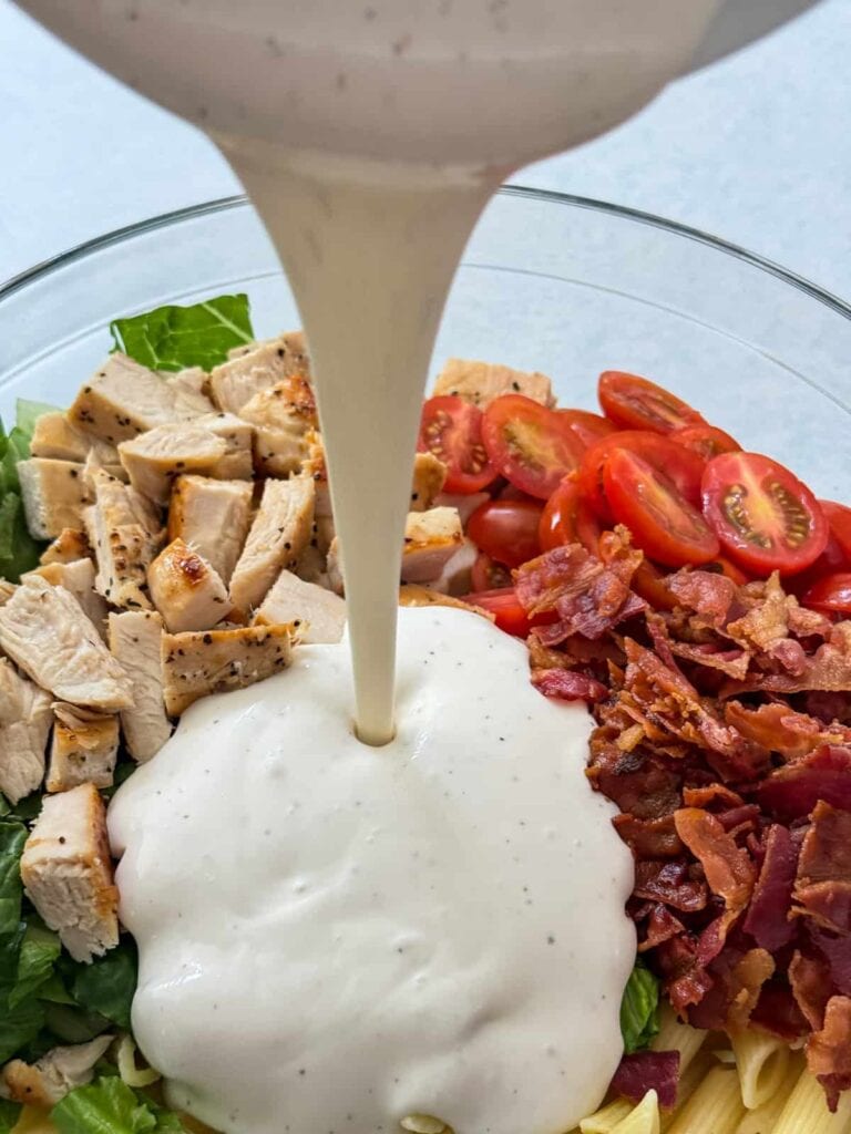 The dressing being poured over the other ingredients in a glass mixing bowl.