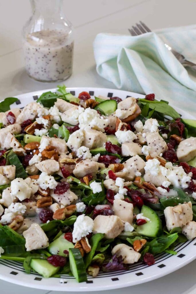 Side view of one plate of Green Salad with Chicken with a small bottle of salad dressing in the background.