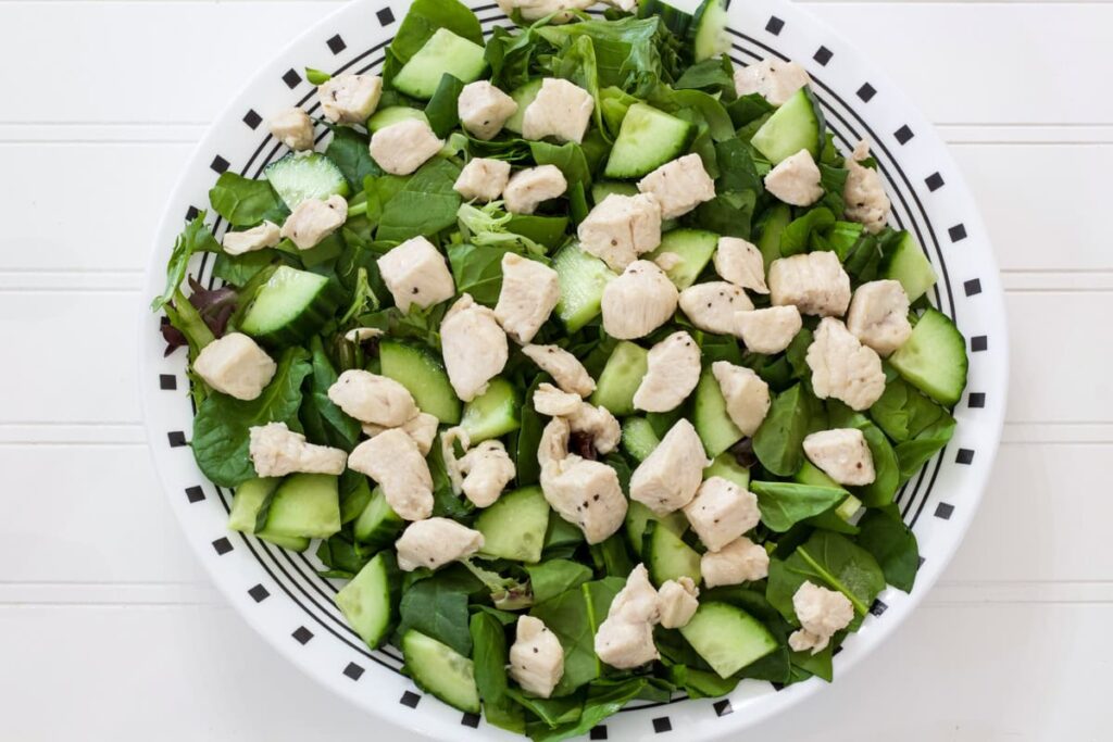 The cucumbers and cooked chicken added to evenly over the mixed greens.
