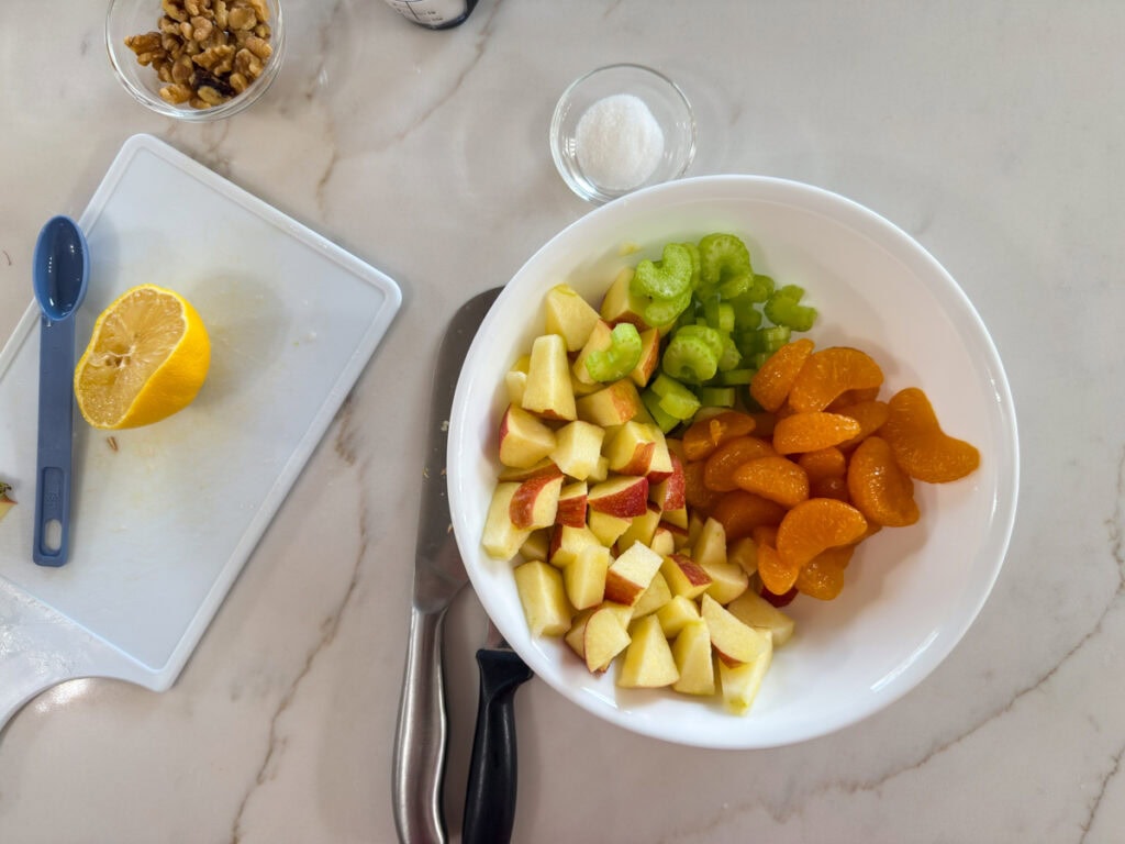 The chopped apple and celery and the mandarin oranges in a white bowl.