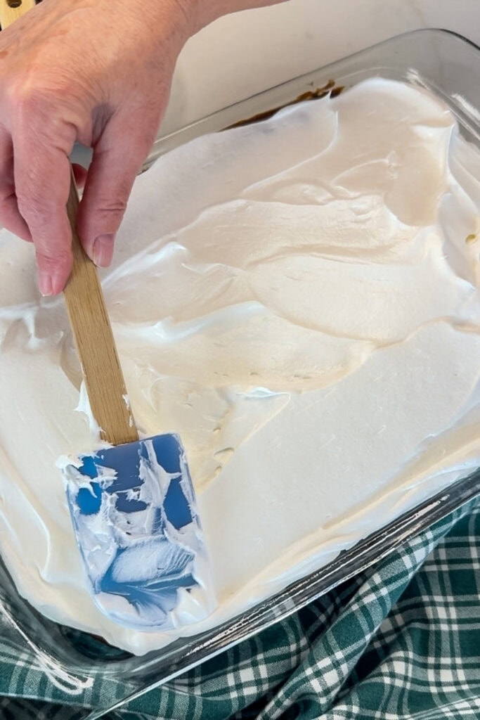 The cool whip layer being spread onto the pudding layer.