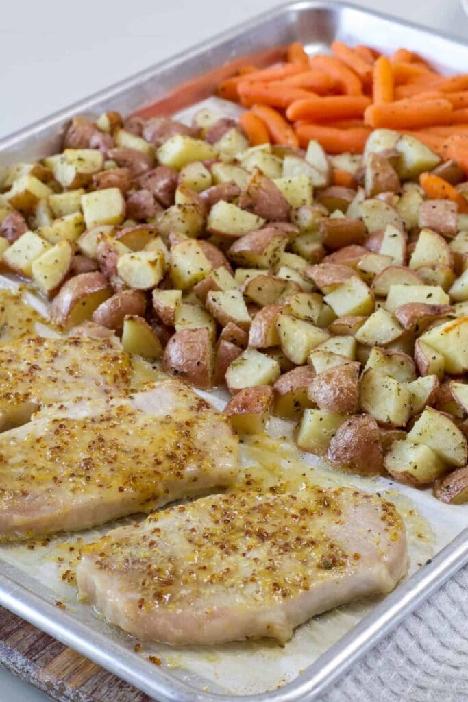 Four pork chops, red potatoes, and petite carrots on a sheet pan after they've been cooked.