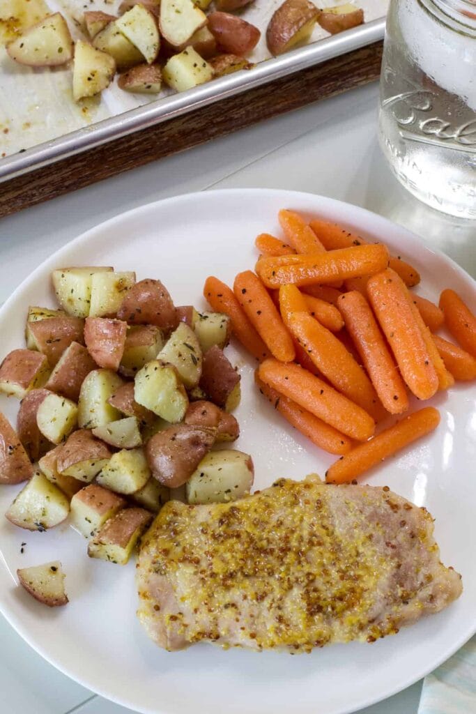 A pork chop, serving of carrots and red potatoes on a white plate.