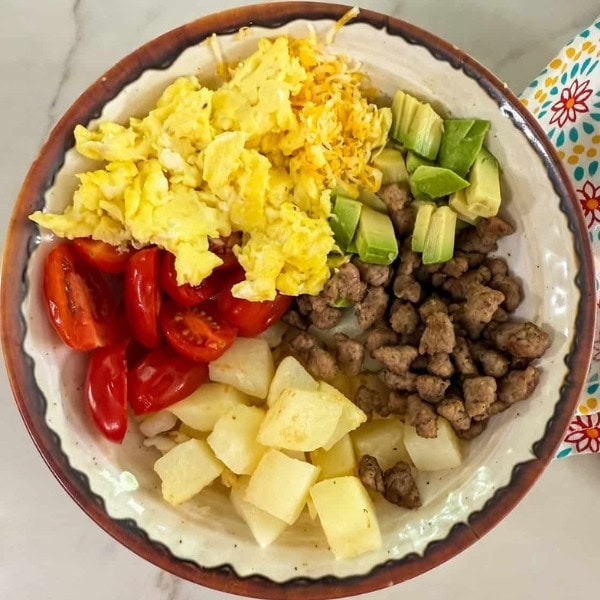 The eggs, sausage, potatoes, tomatoes and avocado in a bowl, ready to be mixed.