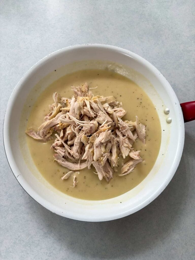 The shredded rotisserie chicken added to the skillet with the gravy, before being mixed up.