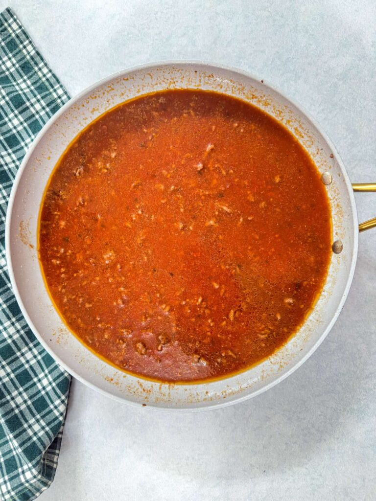 The ground beef, water and marinara sauce in a skillet.