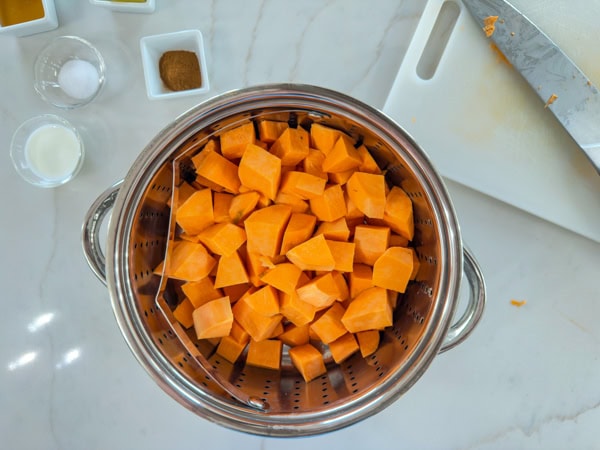 The cubed sweet potatoes in a steamer basket inside a pot.