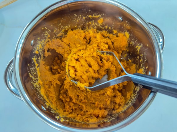 The sweet potatoes after they've been mashed with a potato masher.