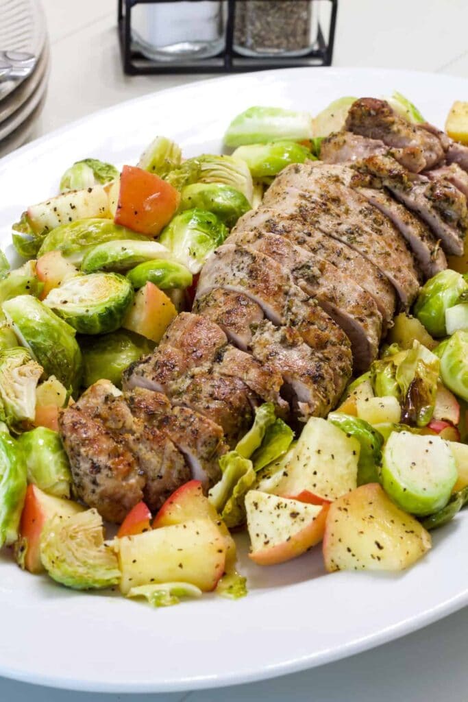 Overhead close up of a roasted pork tenderloin with seasoned apples and Brussels sprouts on a serving platter.