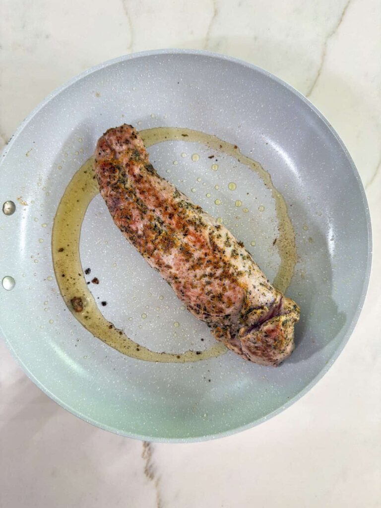 The pork tenderloin in a skillet after it's been seared on all sides.