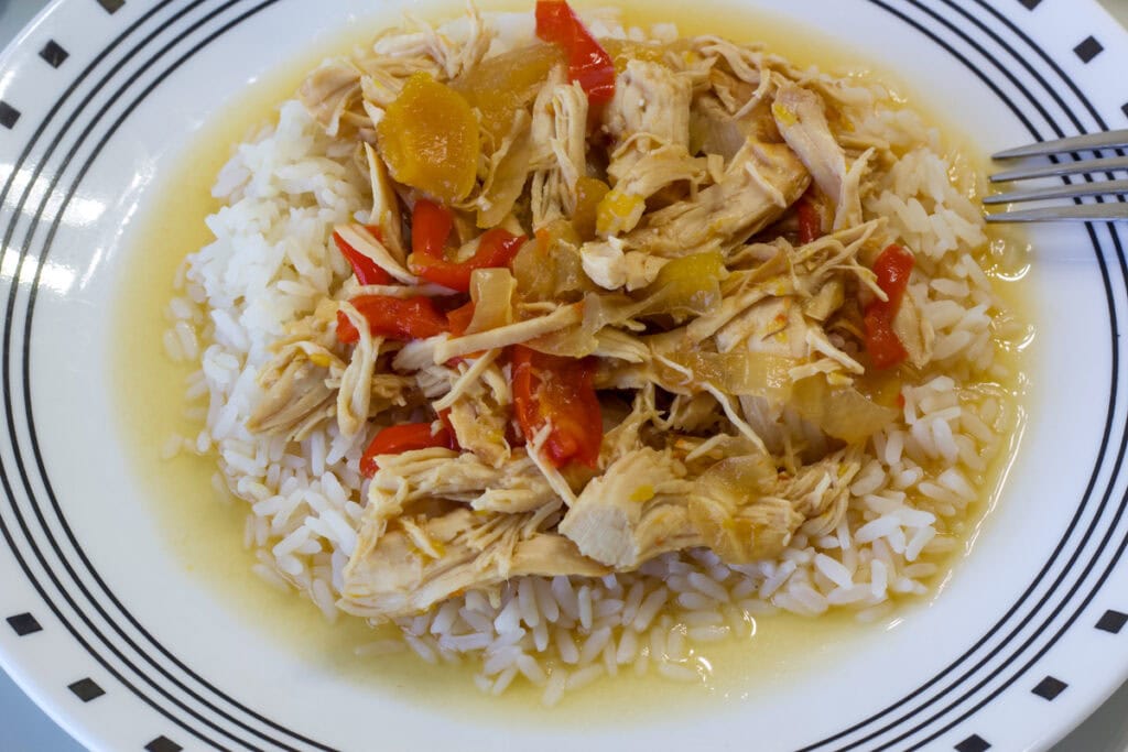 Overhead shot of the Slow Cooker Peach Chicken over white rice on a white plate that has black accents.