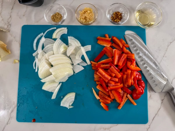 The onion and red bell pepper cut up on a cutting board.
