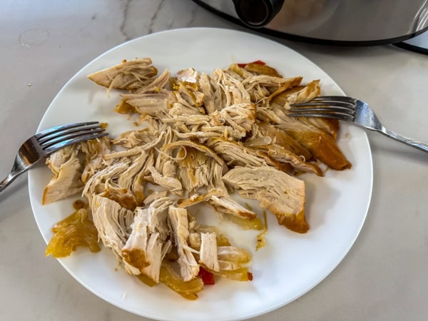 The chicken breasts on a white plate after they've been shredded with two forks.