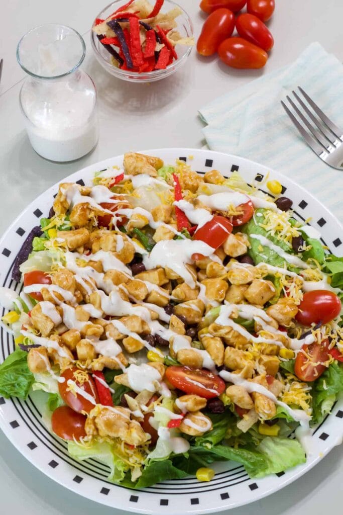 Overhead shot of one Southwest BBQ Chicken Salad and a small bottle of dressing, tortilla strips and a few cherry tomatoes.