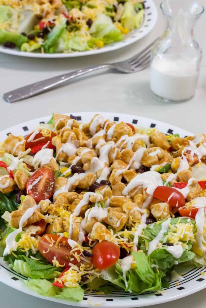 Close up side view of the romaine lettuce, topped with corn, beans, bbq chicken, cherry tomatoes, cheese and dressing.
