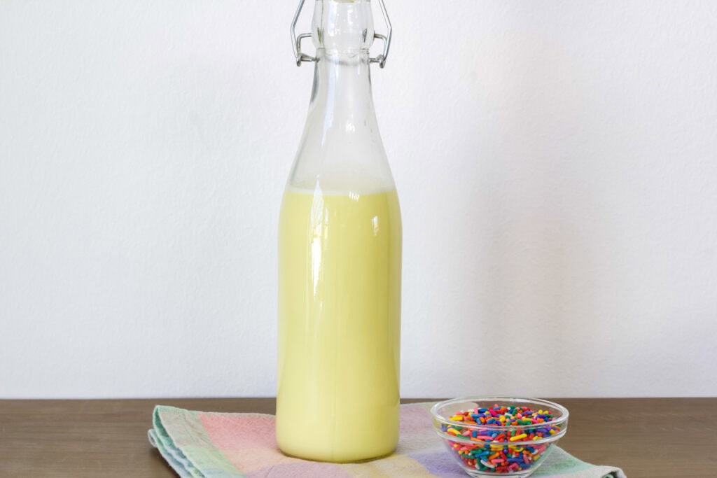 A glass bottle of Birthday Cake Coffee Creamer and a small bowl of rainbow sprinkles.