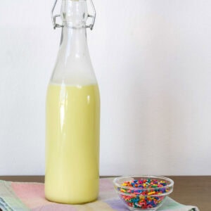 Side view of the bottle of homemade Birthday Cake Coffee Creamer and a small bowl of sprinkles.