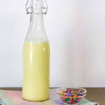 Side view of the bottle of homemade Birthday Cake Coffee Creamer and a small bowl of sprinkles.