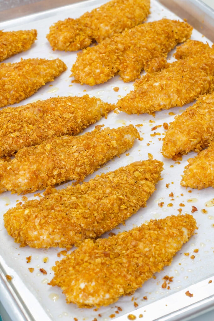 The Crispy Baked Cornflake Chicken Strips on a rimmed baking sheet after they've came out of the oven.