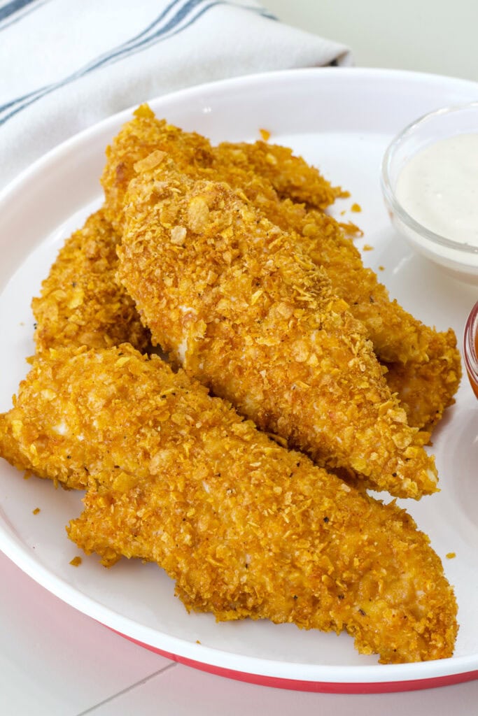 Several Crispy Baked Cornflake Chicken Strips on a white and red plate ready to be served.
