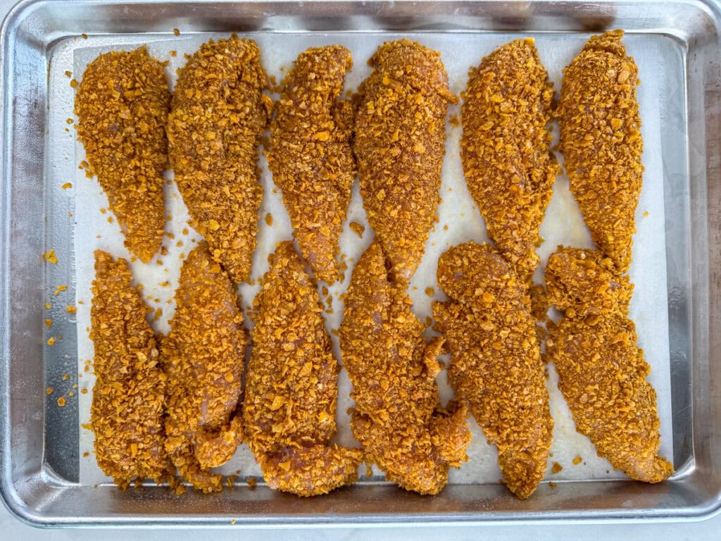 The coated chicken tenders on a rimmed baking sheet ready to go into the oven.