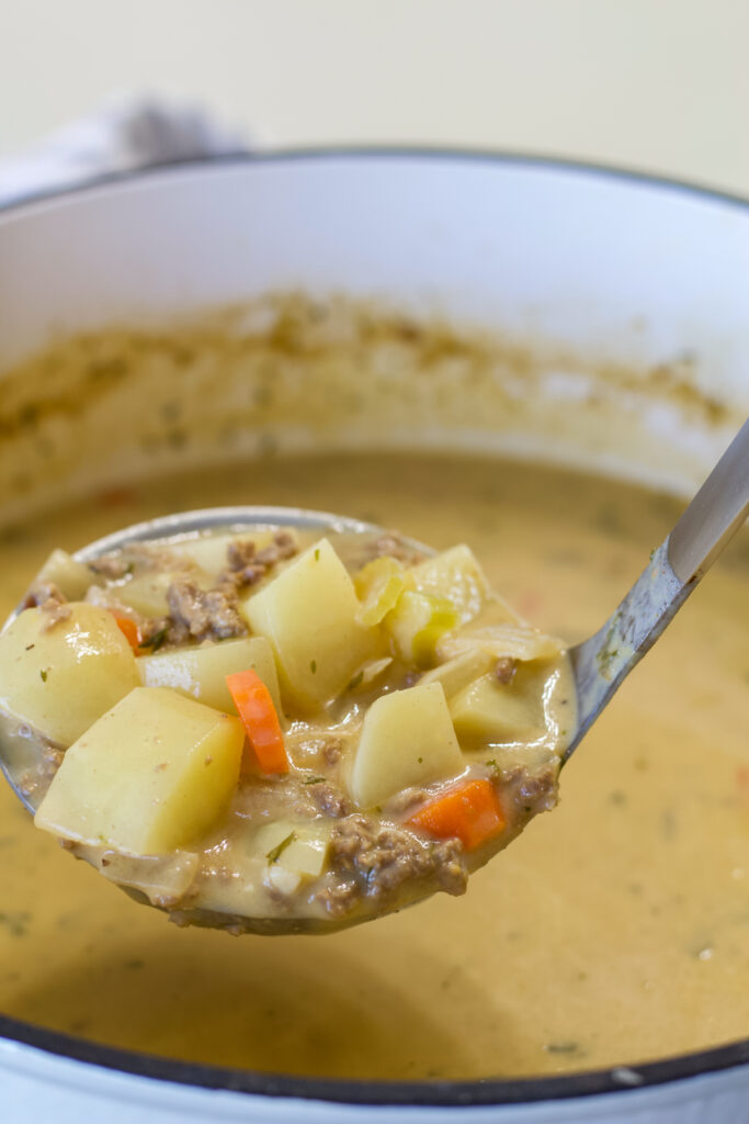 Close up side view of a ladle full of Easy Cheeseburger Soup with Dill Pickles.