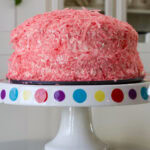 Close up side view of the frosted cake covered with pink coconut flakes.