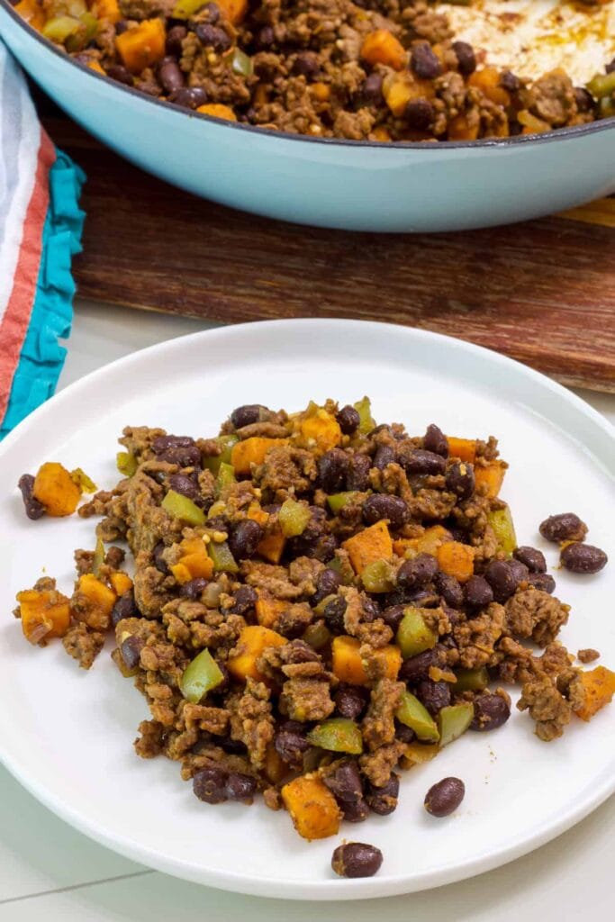 A serving of Ground Beef Sweet Potato HashGround Beef Sweet Potato Hash on a plate and the skillet with the rest in the background.
