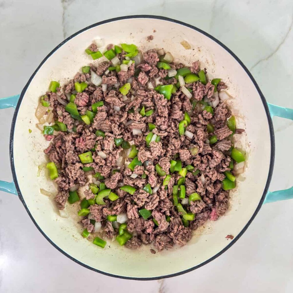 The browned ground beef with chopped bell pepper and onion in the skillet.