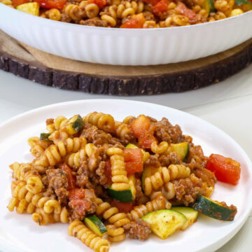 A serving of Pasta with Zucchini and Tomatoes on a plate in the foreground and the skillet with the rest in the background.