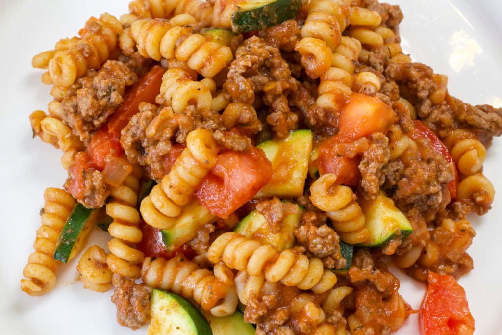 One serving of Pasta with Zucchini and Tomatoes on a white plate.