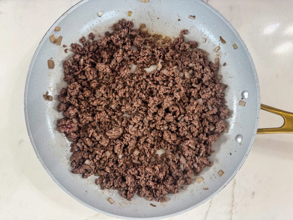 The cooked ground beef and onion in a skillet.