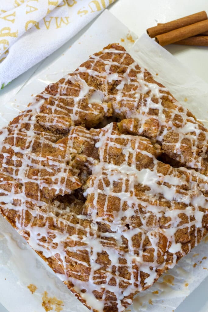 Banana sour cream coffee cake in baking pan topped with cinnamon crumble and vanilla glaze.