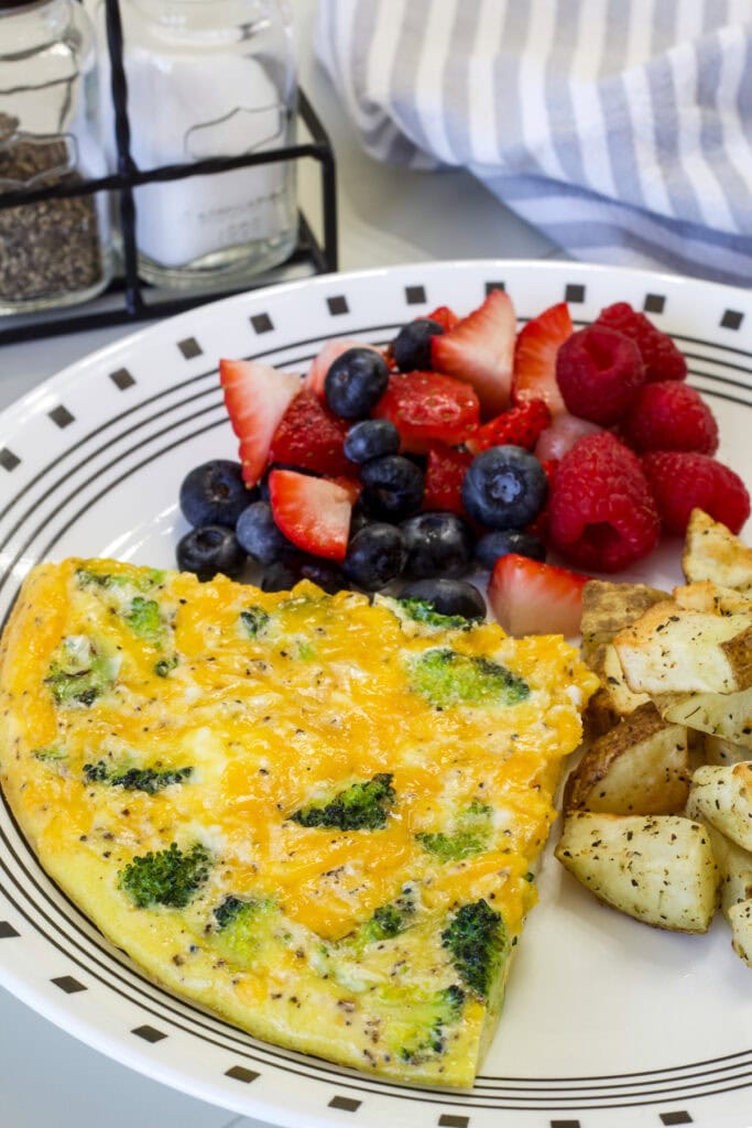 One-fourth of the frittata on a plate with potatoes and fresh fruit.