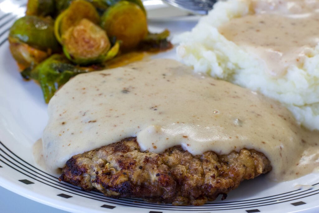One Chicken Fried Steak with Cream Gravy on a plate with mashed potatoes and Brussels sprouts.