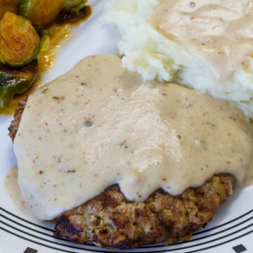 Very close up shot of the Chicken Fried Steak with Cream Gravy over mashed potatoes on a white and black plate.