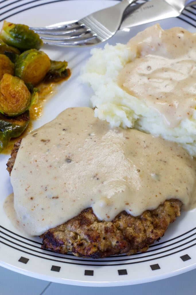 Overhead of Chicken Fried Steak with Cream Gravy over mashed potatoes on a plate with Brussels sprouts.