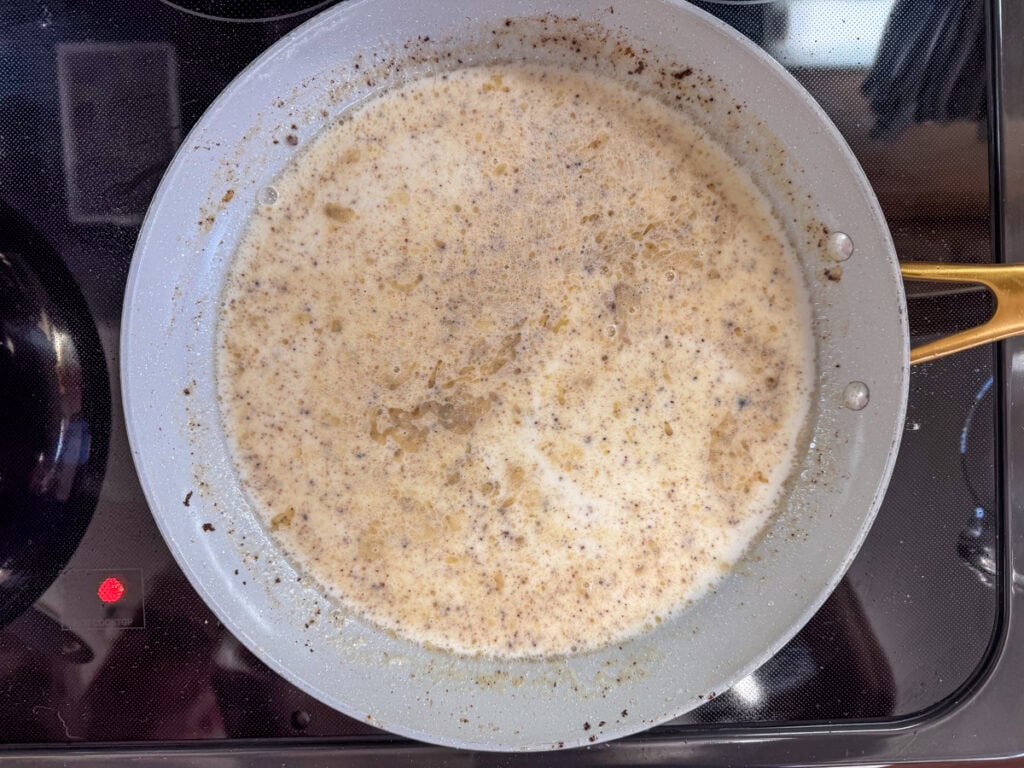 The milk added to the roux in the skillet before it thickens into gravy.