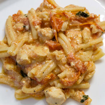 Very close up of a serving of Easy Baked Feta Pasta with Chicken on a white plate.