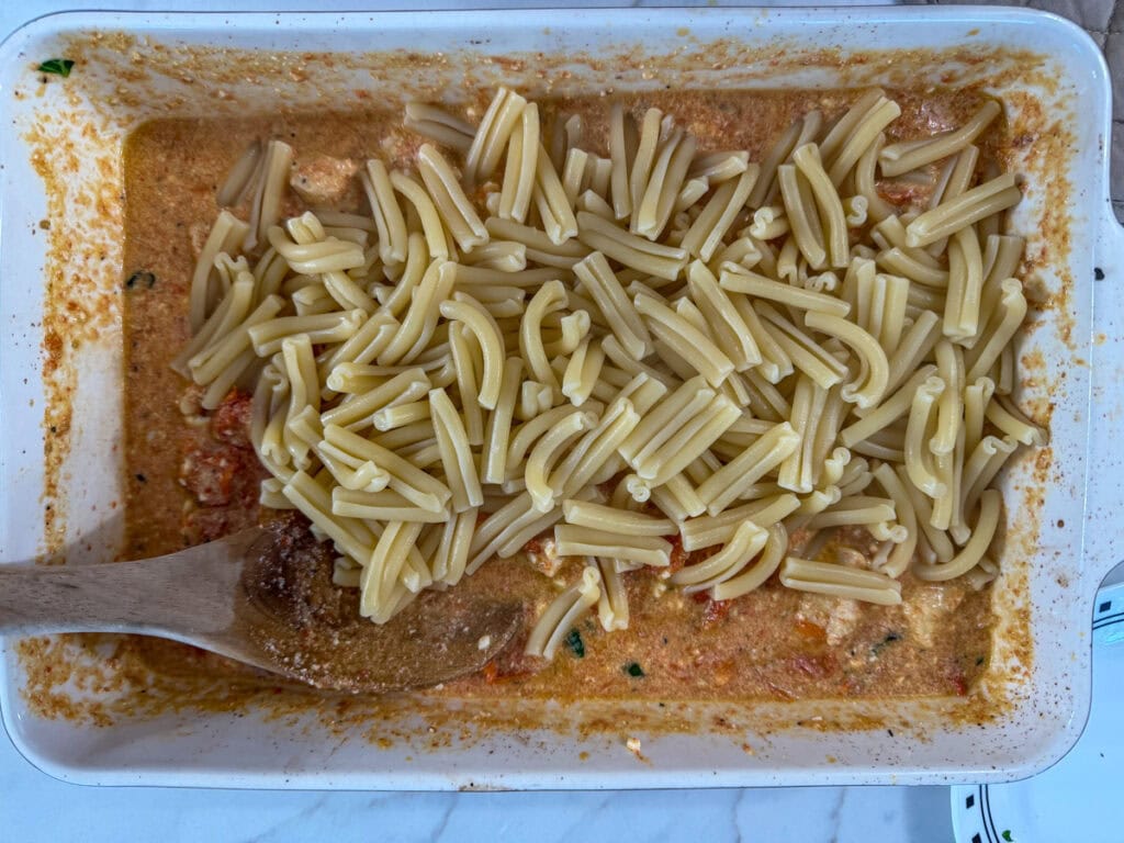 The cooked pasta added to the casserole dish on top of the mixed up sauce.