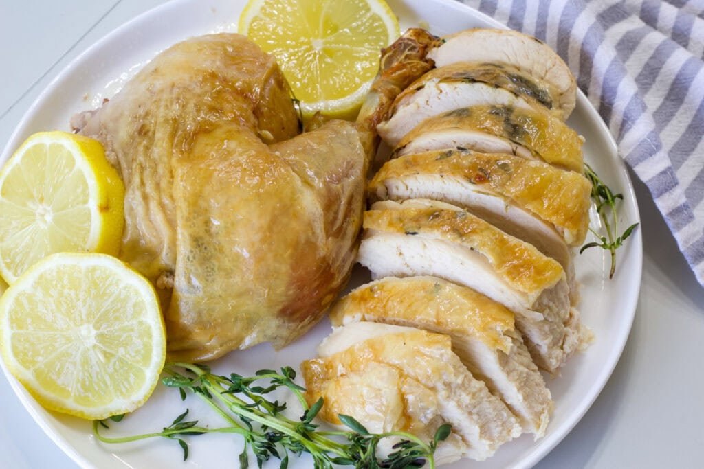 The cut up Lemon and Thyme Roasted Chicken on a white plate with lemon and fresh time sprigs.