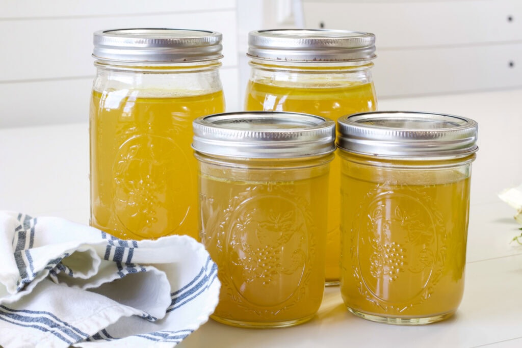 Four mason jars filled with homemade low cooker chicken stock.