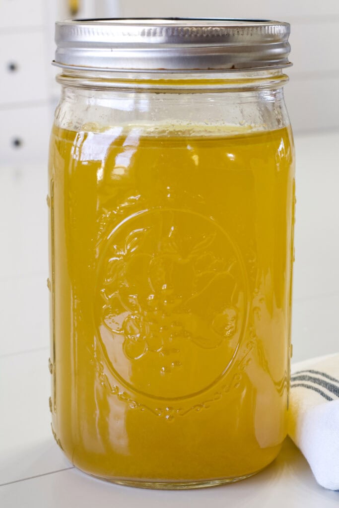 Close up side shot of one large mason jar filled with chicken stock made in the slow cooker.